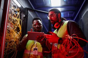 DECU, Retrato de dos técnicos que usan una tableta digital mientras reparan servidores y configuran una red de datos bajo una luz de neón.